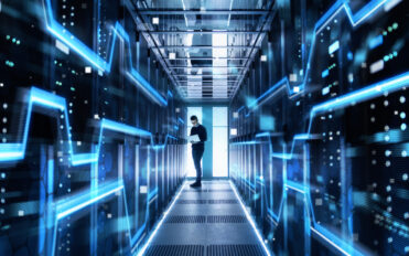 Male IT Engineer Works on a Laptop in a Big Data Center. Rows of Rack Servers are Seen.